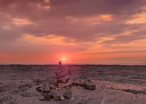 Sunset from a lava field of the older Mauna Loa eruptions with a rock stack in the foreground.
